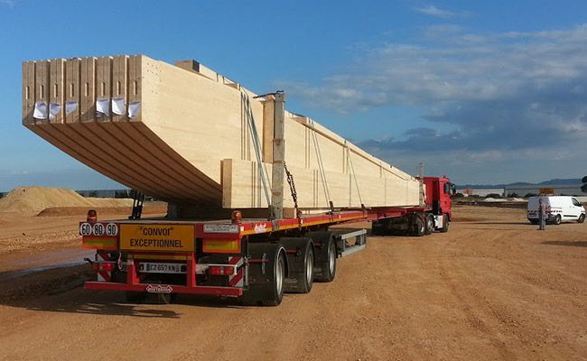 Un camion transportant une cargaison de longues planches de bois empilées par une journée ensoleillée.