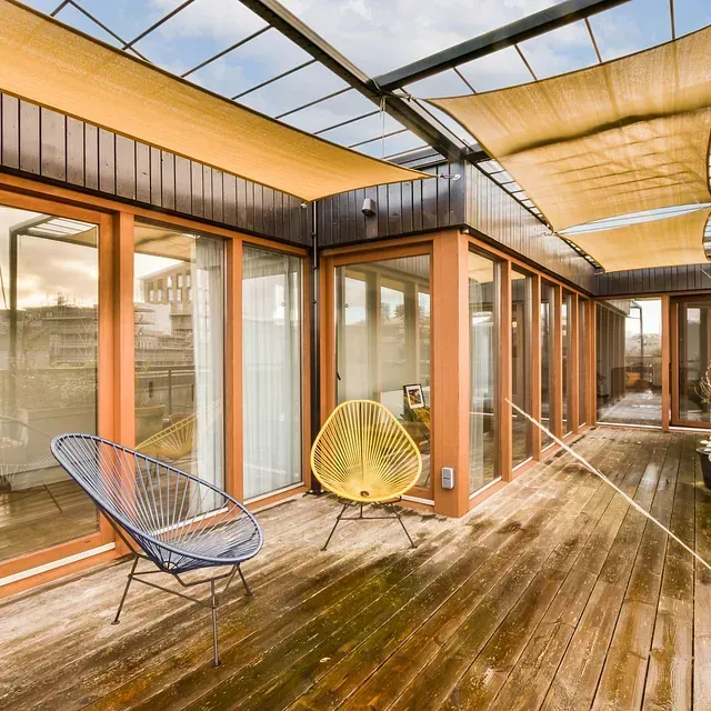 Una terraza de madera con sillas y una gran ventana.