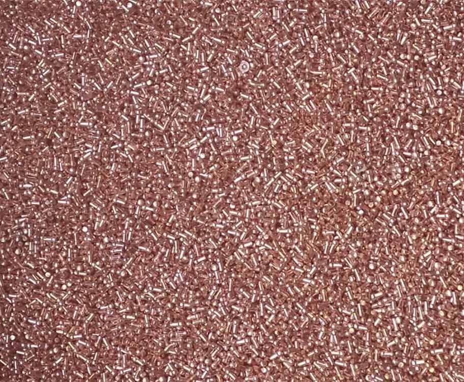 Vista de cerca de muchas cuentas pequeñas, de forma cilíndrica, de color oro rosa.