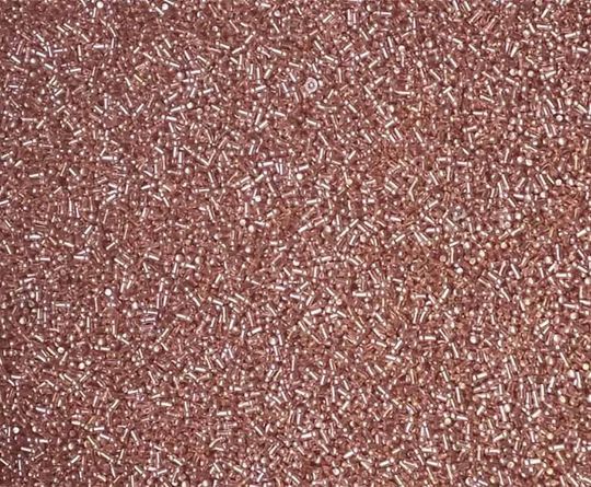 Vista de cerca de muchas cuentas pequeñas, de forma cilíndrica, de color oro rosa.