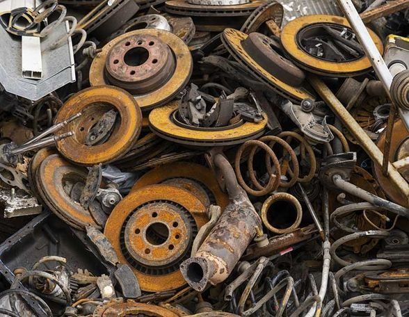 Pila de piezas de automóvil oxidadas, incluidos rotores de freno, resortes y componentes de escape.