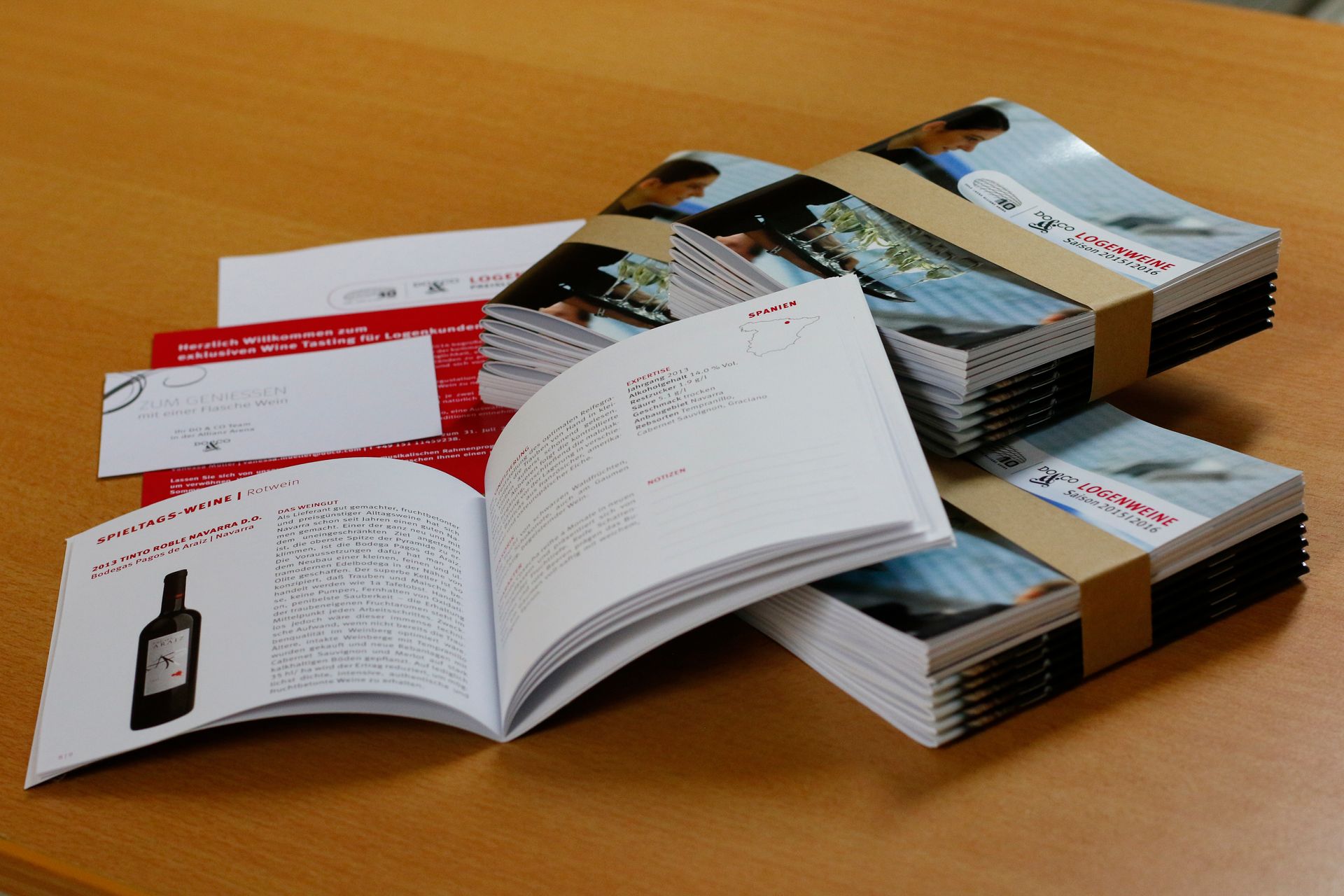 Ein Stapel Bücher auf einem Tisch, eines davon ist auf einer Seite aufgeschlagen, auf der eine Flasche steht