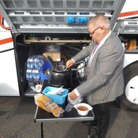 Mann verteilt Essen neben einem Bus mit offener Gepäckklappe