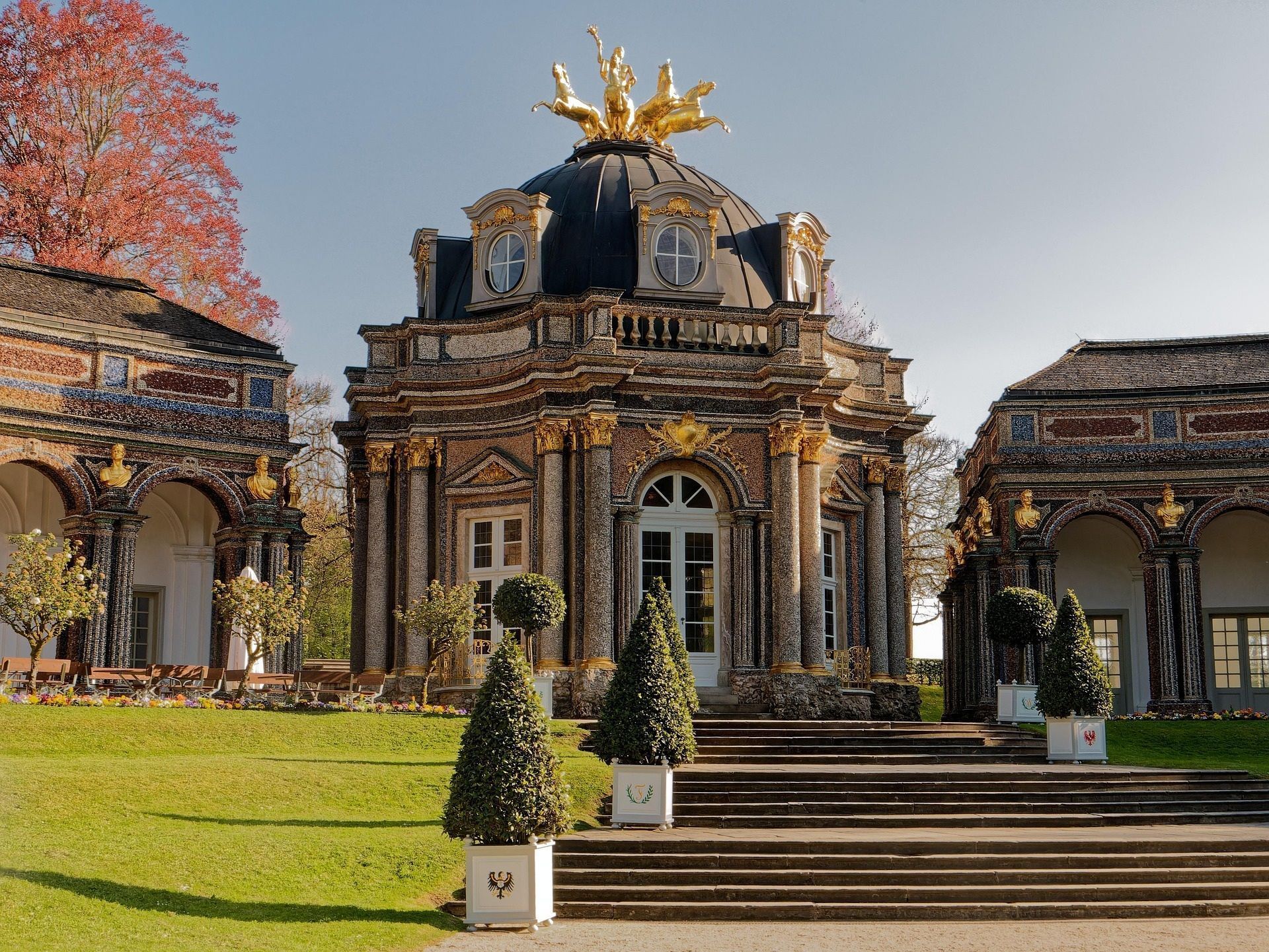 Prunkvoller Barockpavillon mit goldenen Akzenten und Kuppel in parkähnlicher Umgebung.