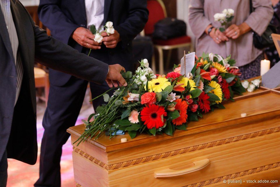 Menschen legen bei einer Beerdigung Blumen auf einen Holzsarg.