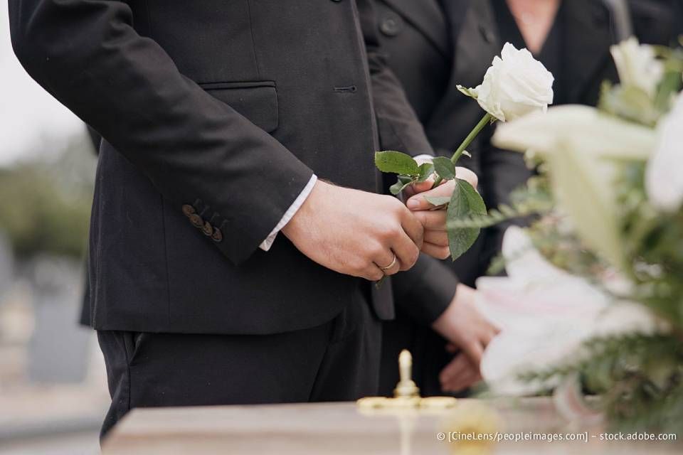 Eine Person im schwarzen Anzug hält bei einer Beerdigung eine weiße Rose.