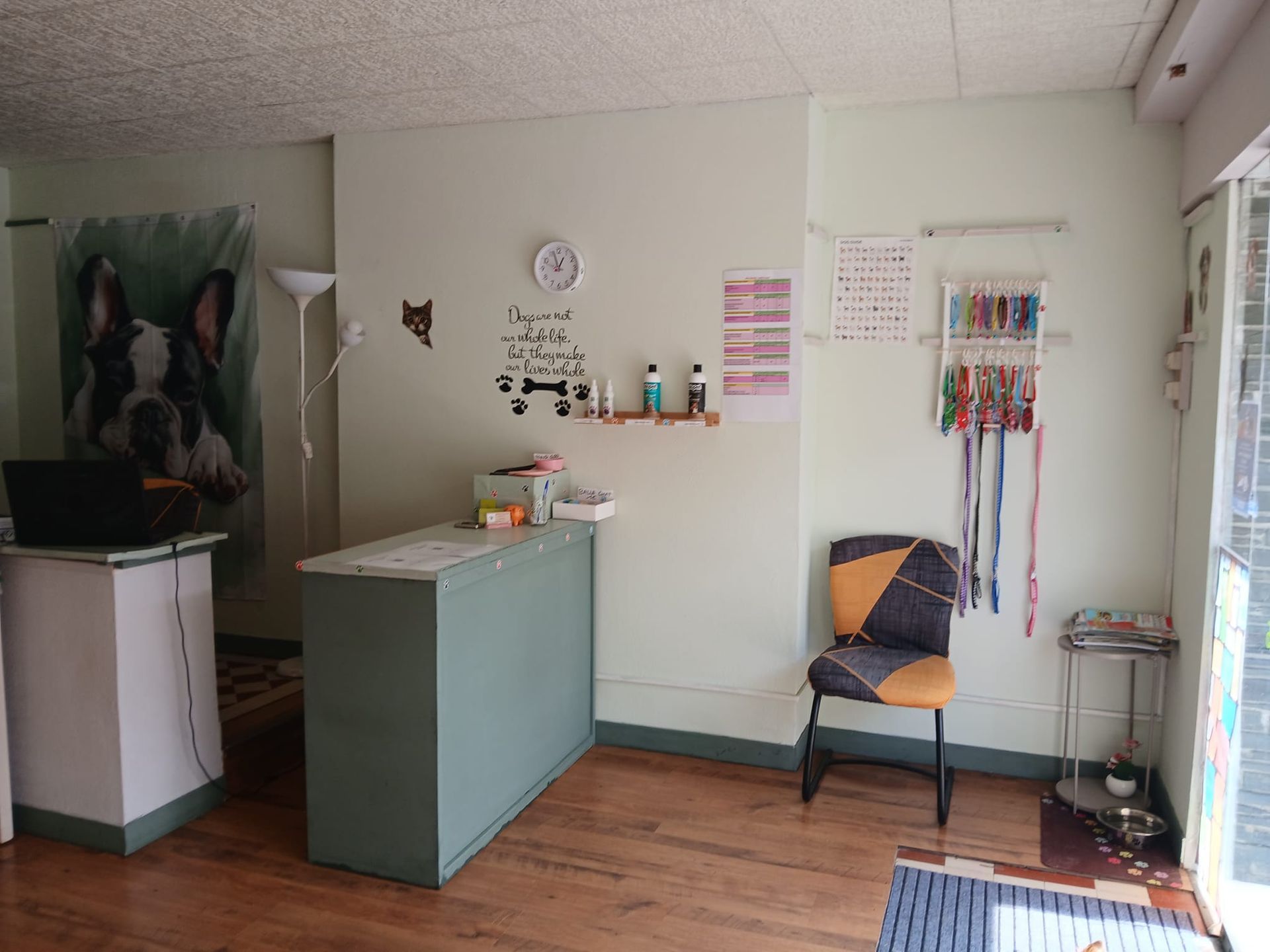 Petite salle d'attente avec bureau, chaise, horloge murale et rubans colorés sur un présentoir.