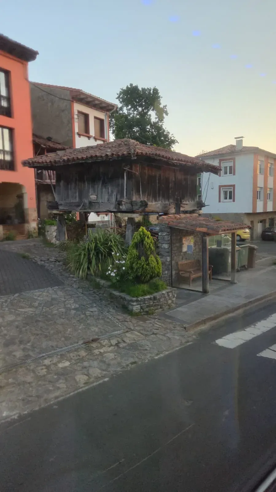 Antigua casa de madera en una empinada calle empedrada, con edificios coloridos y un cielo vespertino tranquilo.