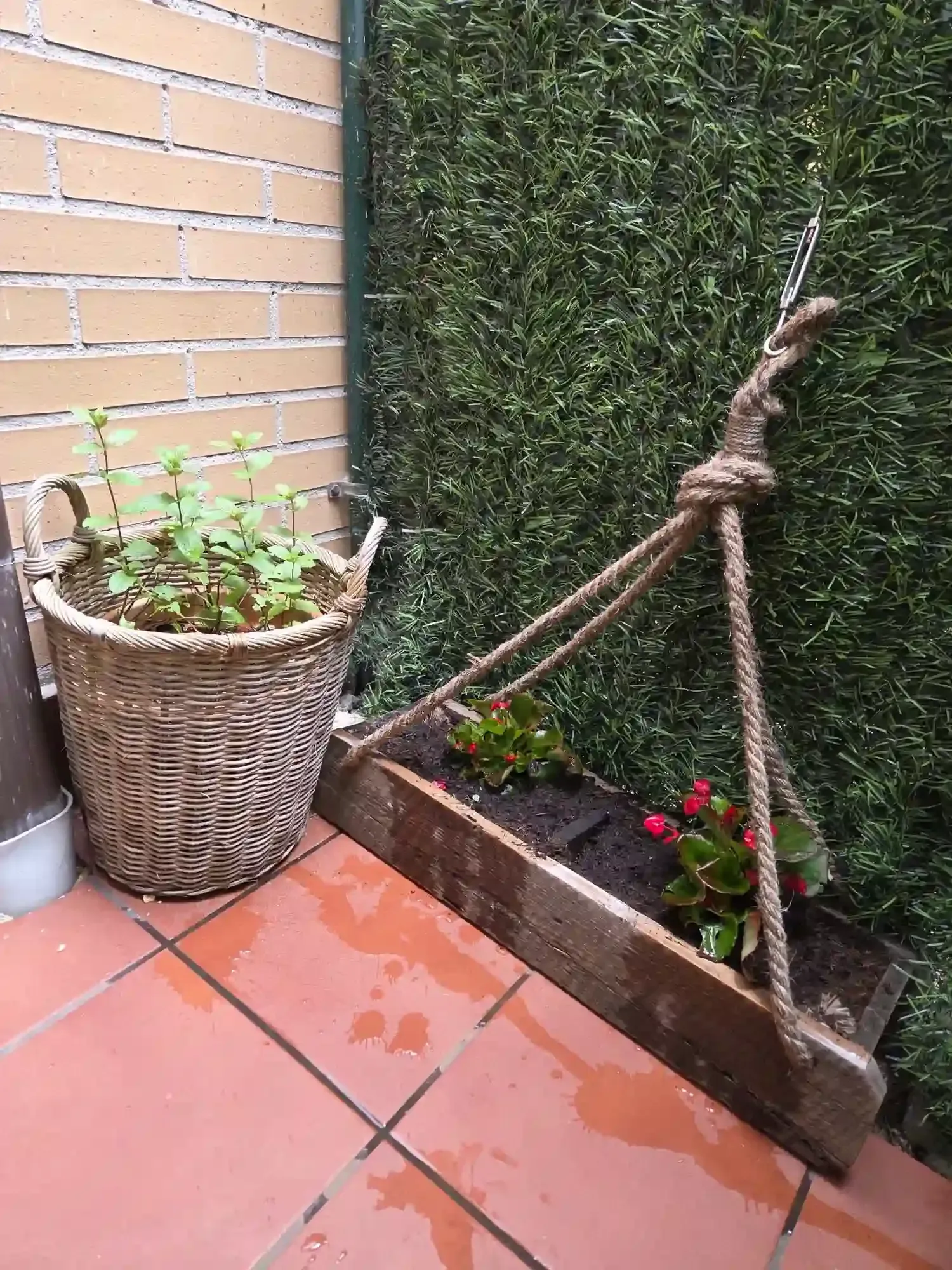 Pequeño patio con una jardinera de mimbre, un parterre elevado y un soporte de madera