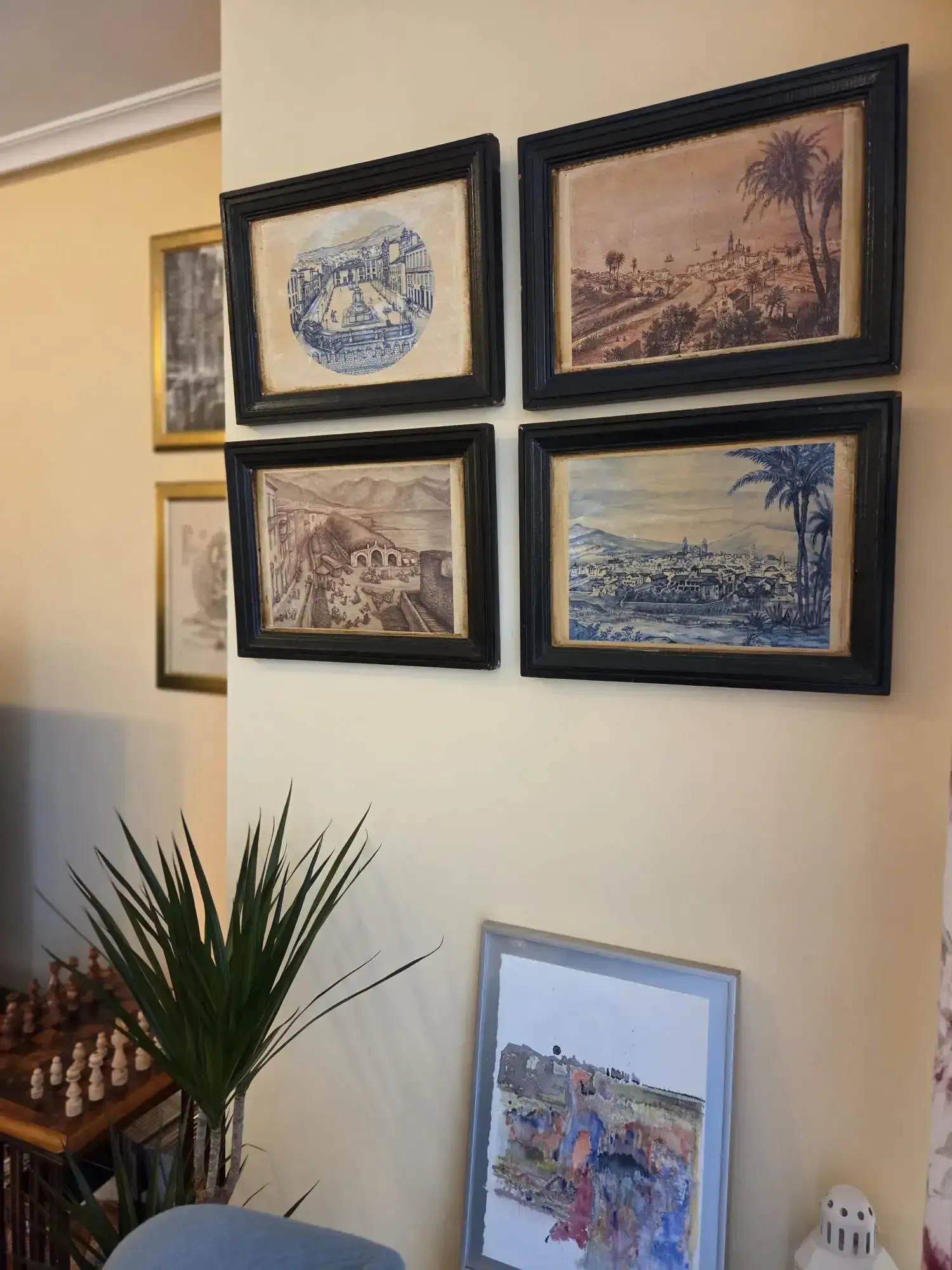 Galería de obras de arte náuticas enmarcadas en la pared sobre una planta en una habitación de tonos cálidos.
