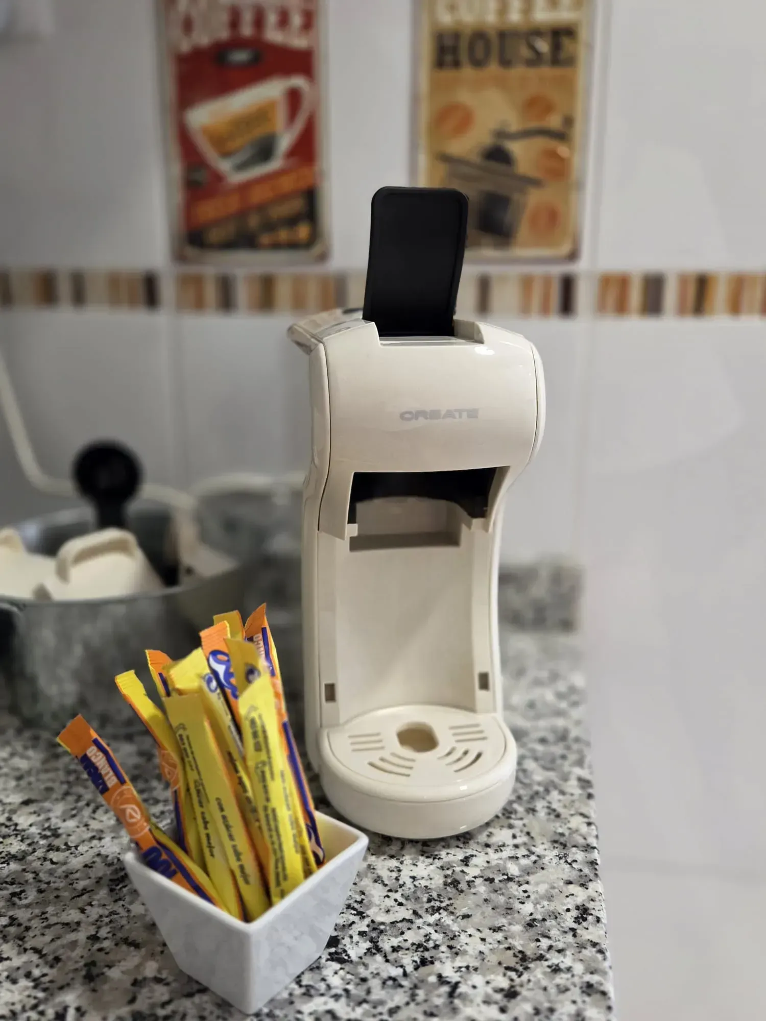 Cafetera sobre una encimera moteada junto a un vaso con sobres de azúcar en una cafetería.