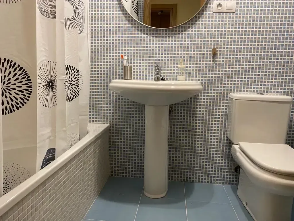 Baño pequeño con paredes de mosaico, lavabo con pedestal, inodoro y cortina de ducha.