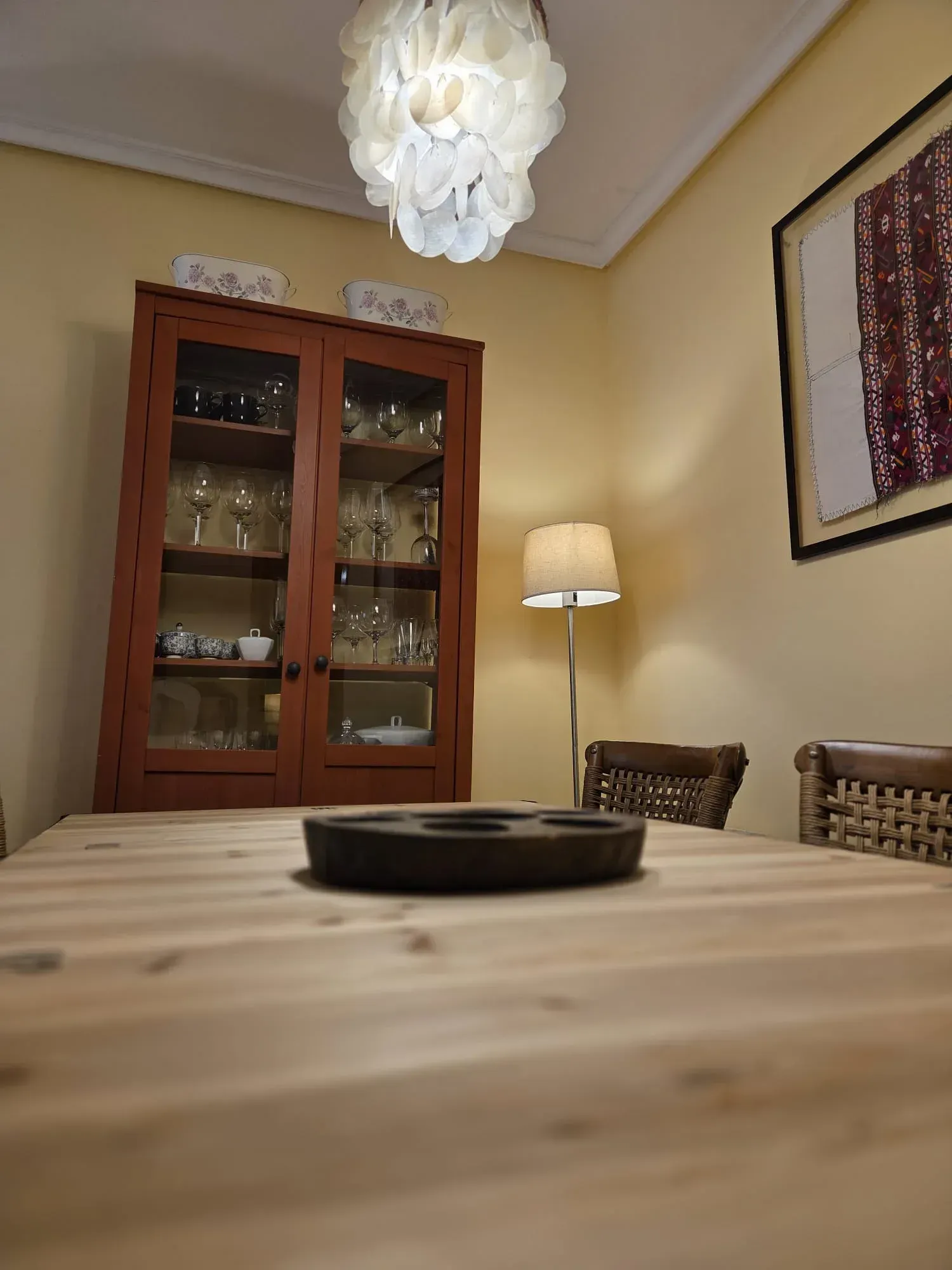 Comedor con mesa de madera, vitrina, lámpara de pie y lámpara colgante blanca.