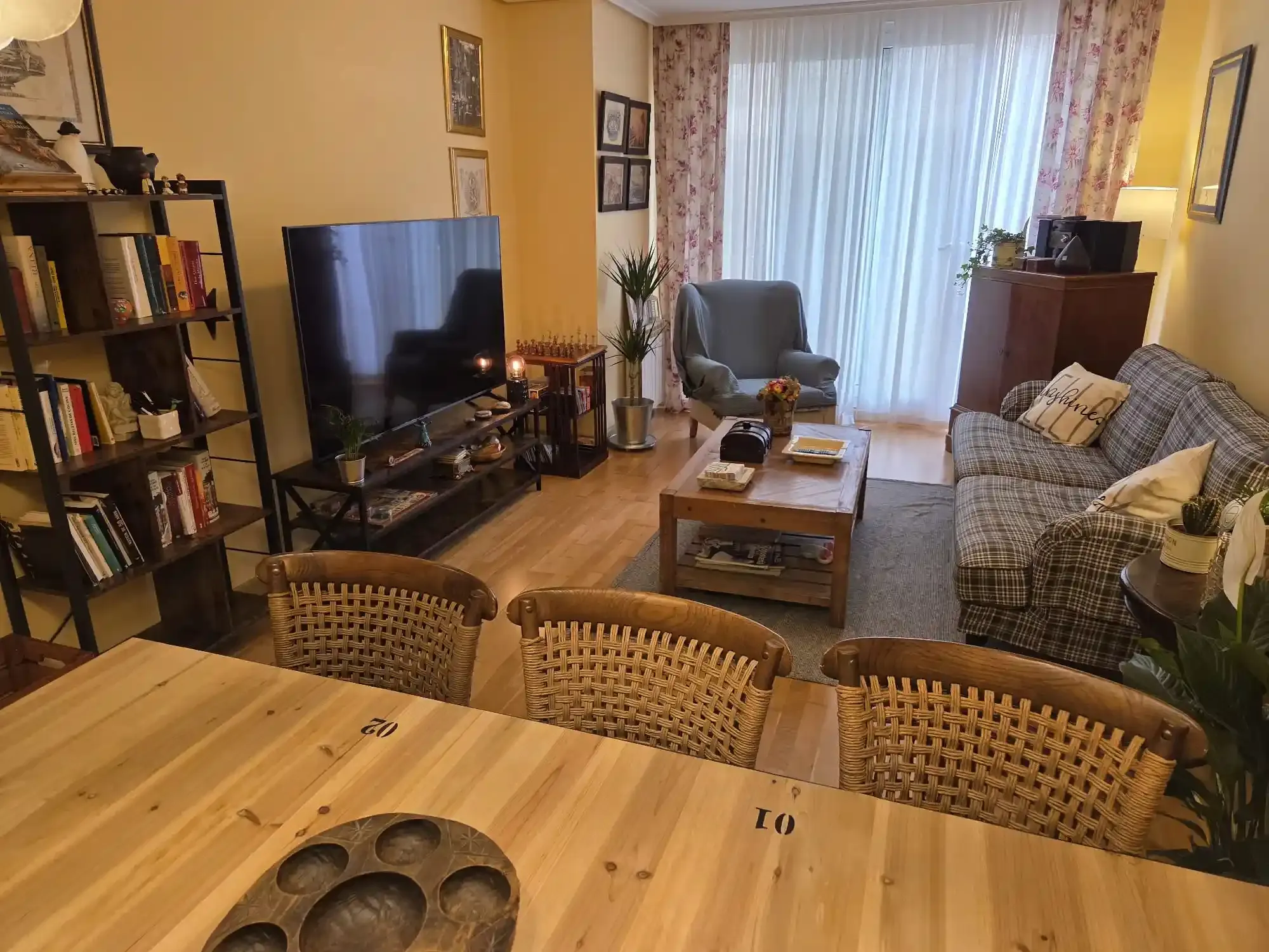 Acogedora sala de estar con televisor, sofá, sillón, mesa de centro, estantería y mesa de comedor en primer plano.