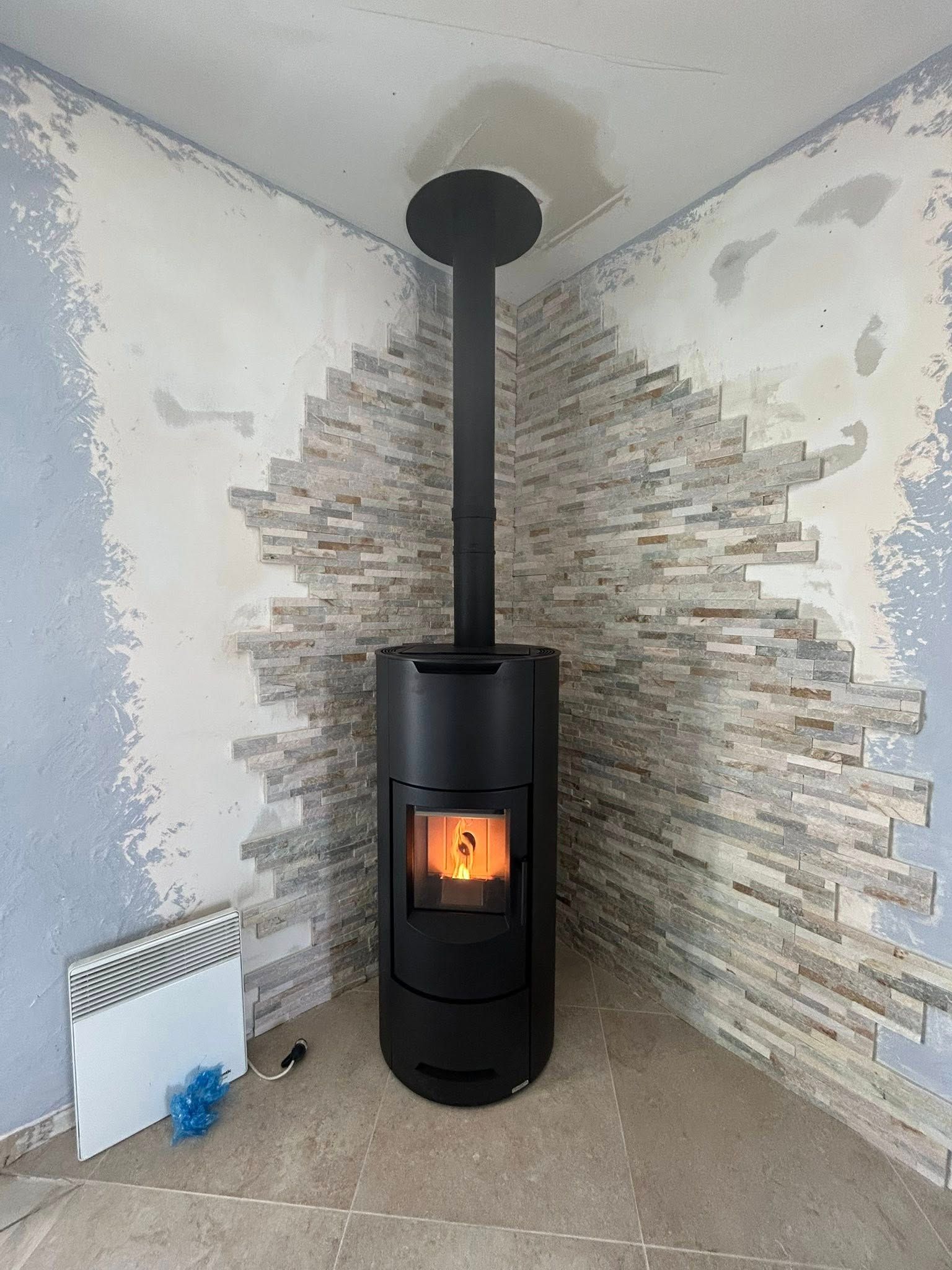 Poêle à bois noir avec un feu crépitant dans l'angle d'une pièce aux murs en pierre.