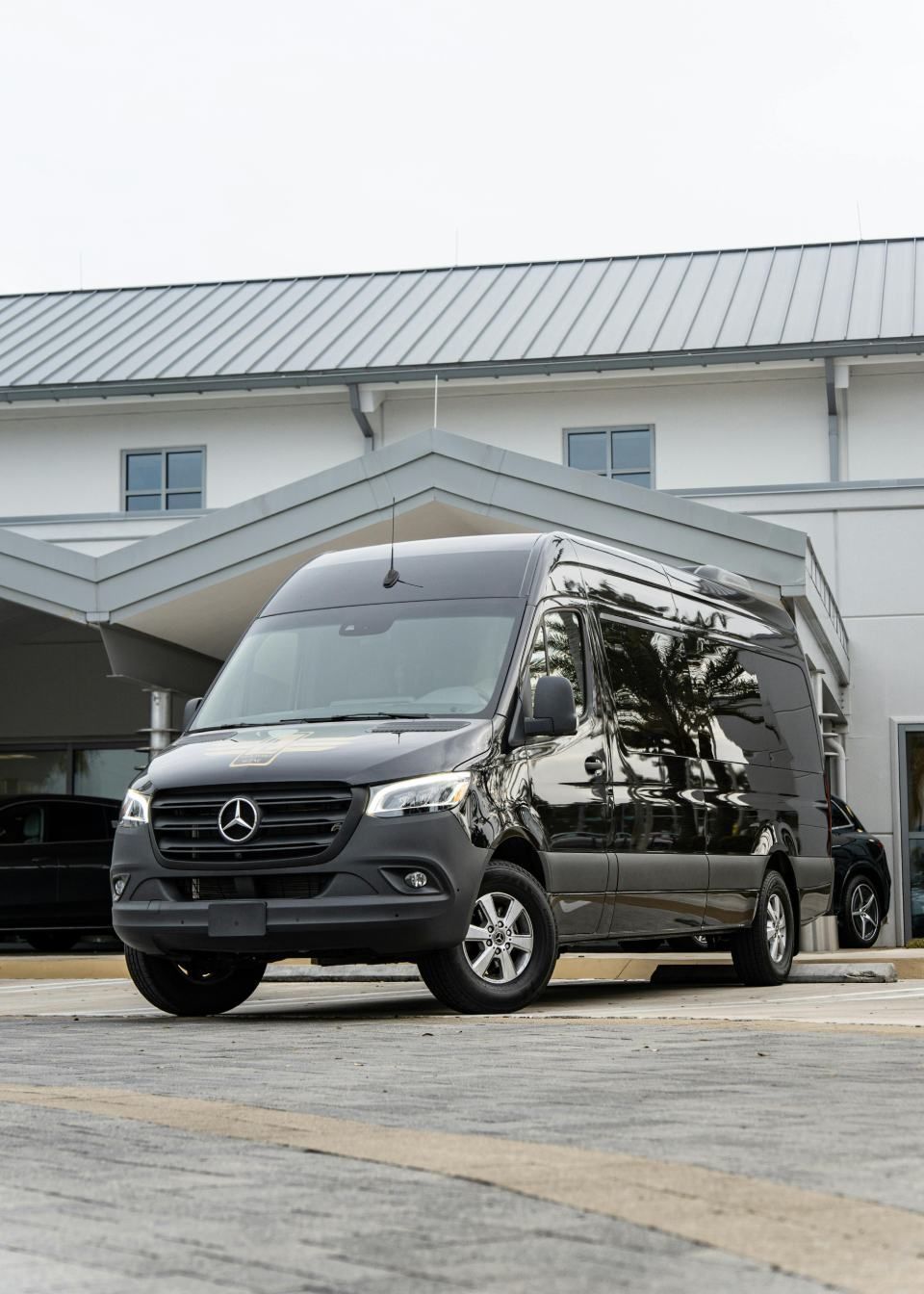 Ein schwarzer Mercedes-Transporter parkt vor einem Gebäude unter einem überdachten Eingang.