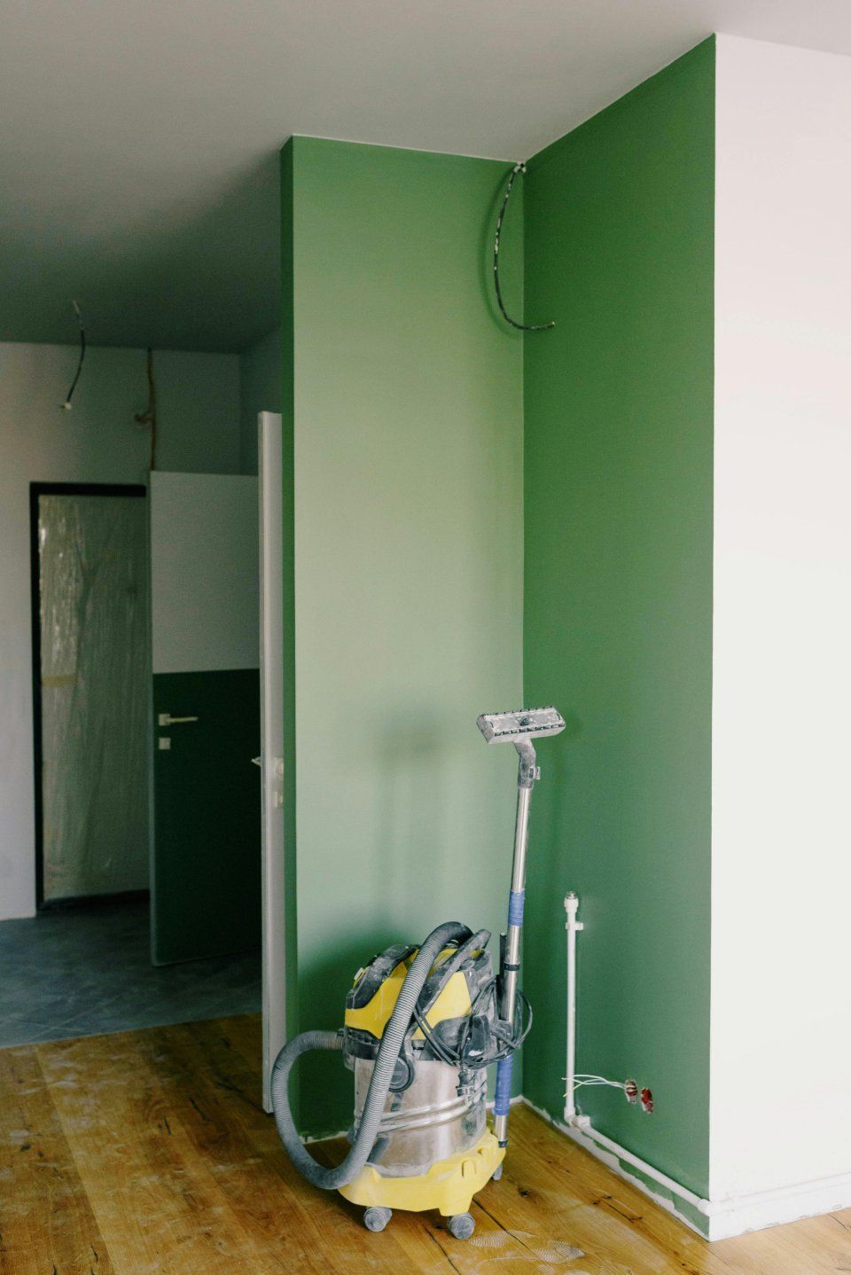 Staubsauger auf Holzboden neben grüner Wand in einem Flur, der renoviert wird