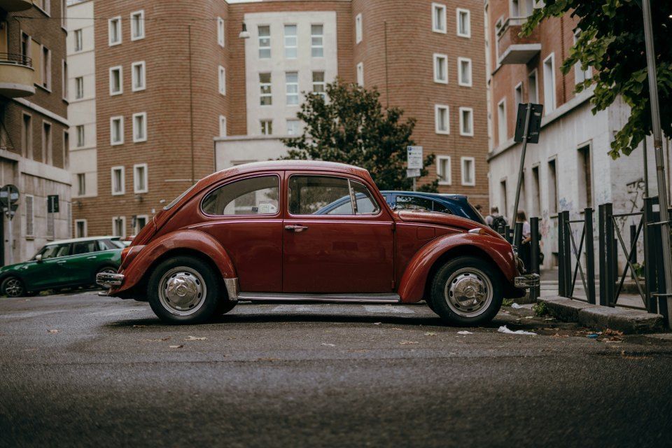 Ein roter Oldtimer-Volkswagen-Käfer parkt auf einer Strasse zwischen Wohnhäusern.