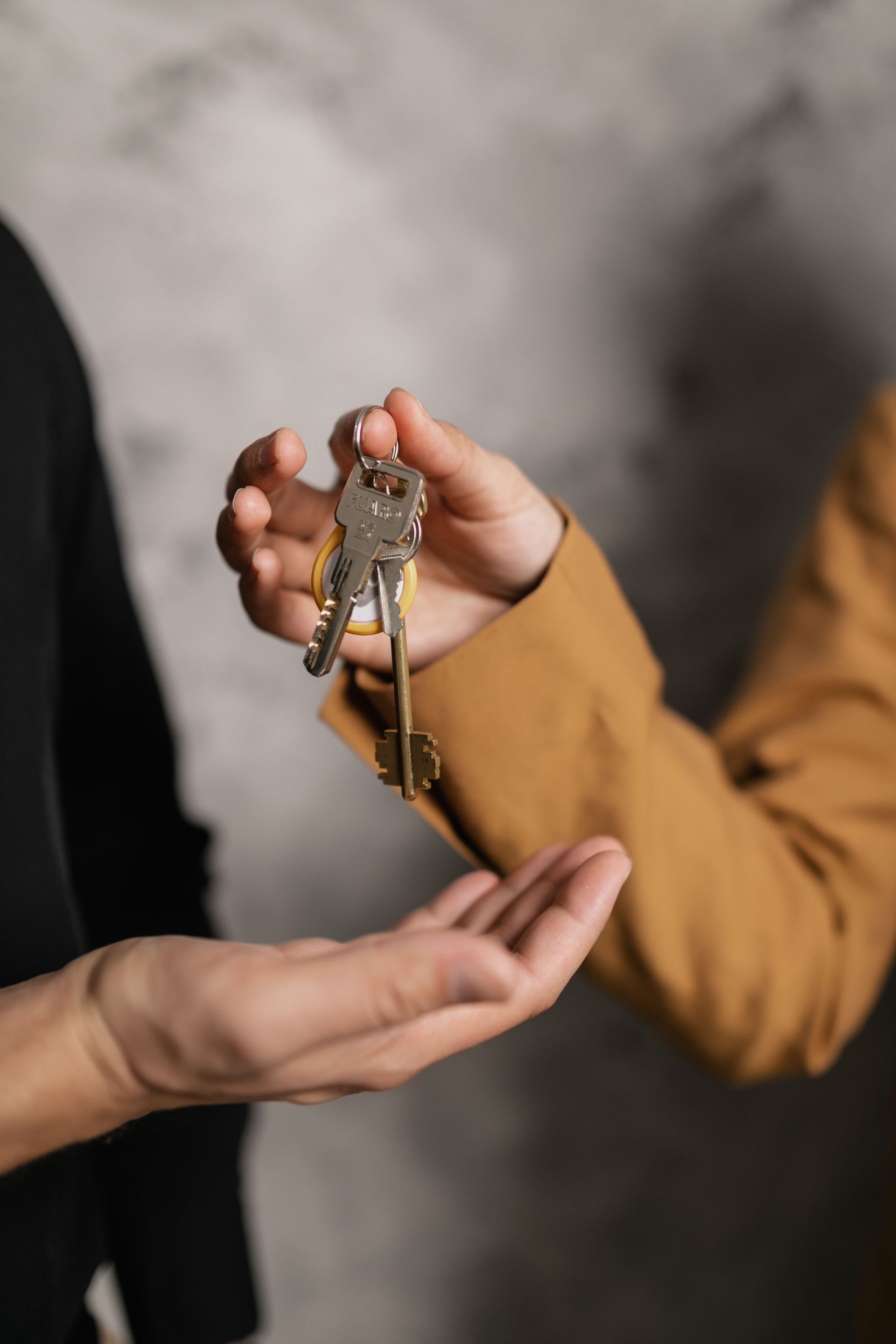 Main tenant une clé de maison au-dessus d'une paume ouverte, avec des personnes floues en arrière-plan