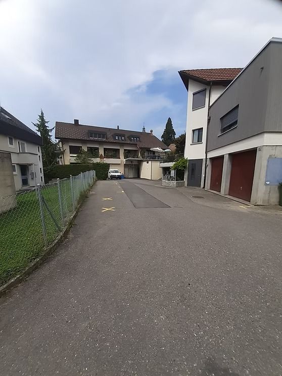 Ruhige Wohnstraße mit Mehrfamilienhäusern, einem geparkten Lieferwagen und einer gepflasterten Zufahrt unter bewölktem Himmel