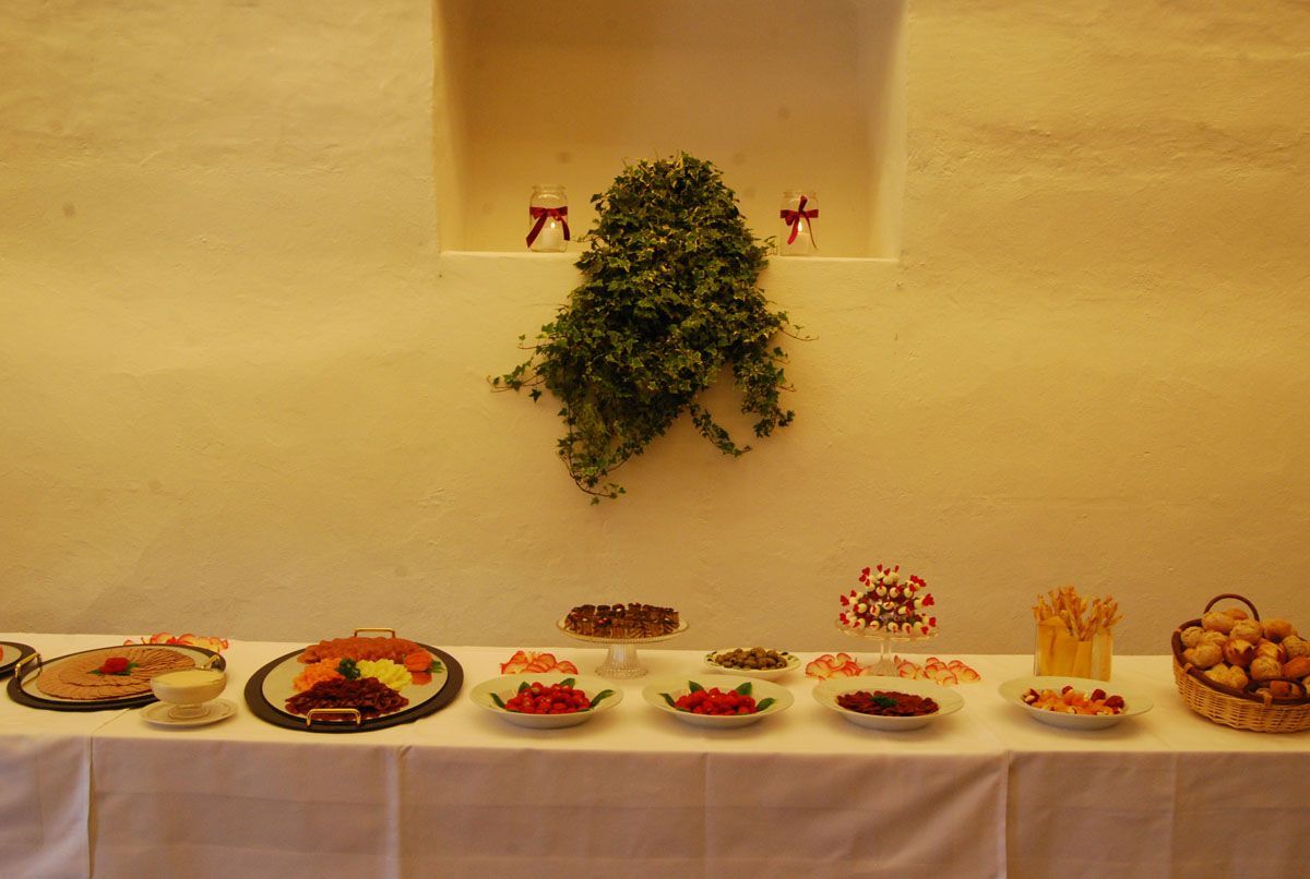 Ein langer Buffet-Tisch mit verschiedenen Desserts unter einer Wandpflanze in einem warm beleuchteten Raum