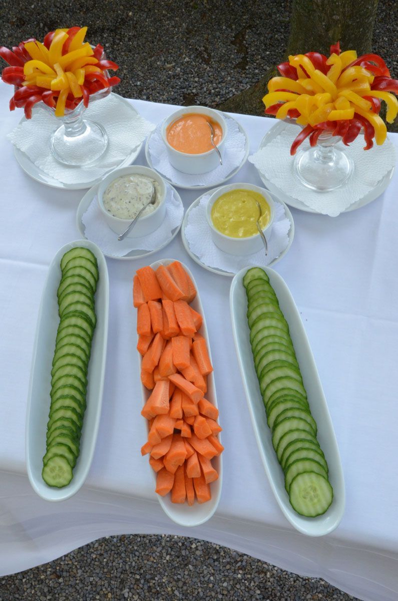 Tischpräsentation mit geschnittenen Gurken und Karotten sowie Dip-Saucen und dekorativen Blumenarrangements.