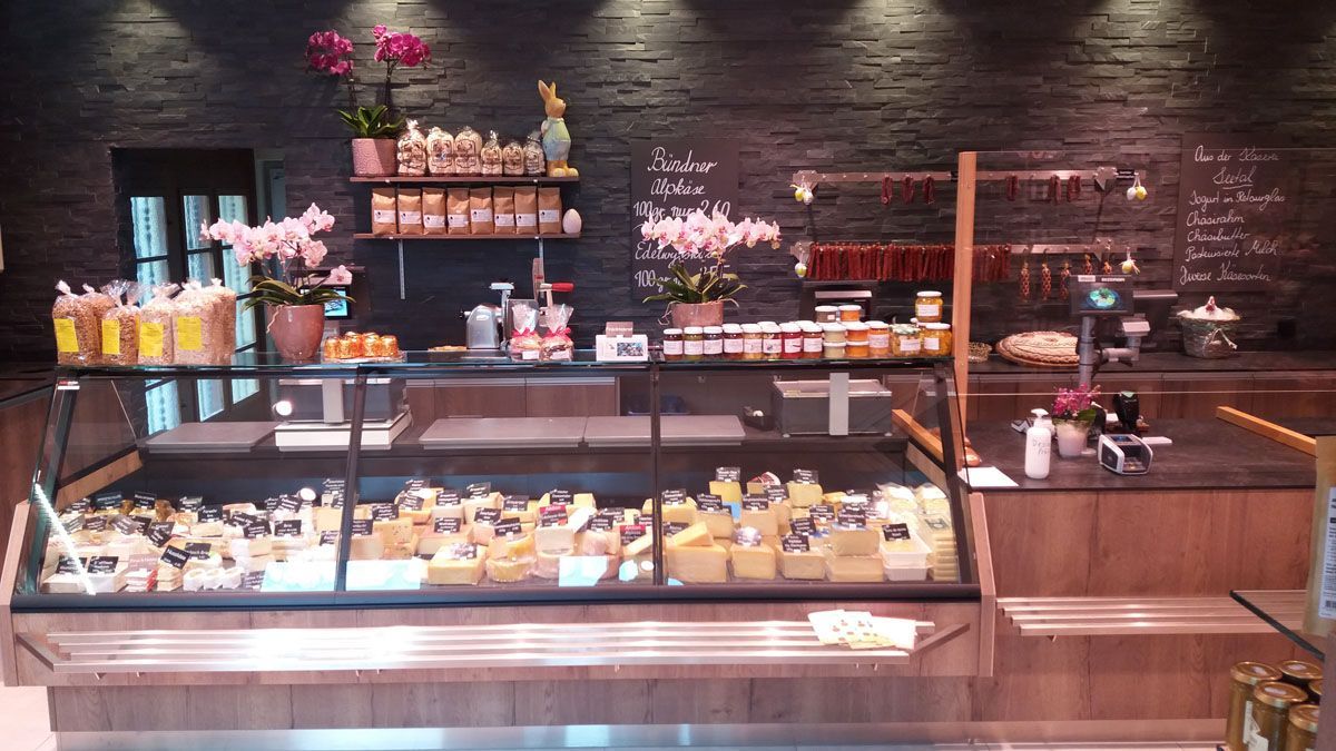 Bäckerei-Vitrine mit Gebäck, Kuchen und Blumen vor einer Backsteinwand