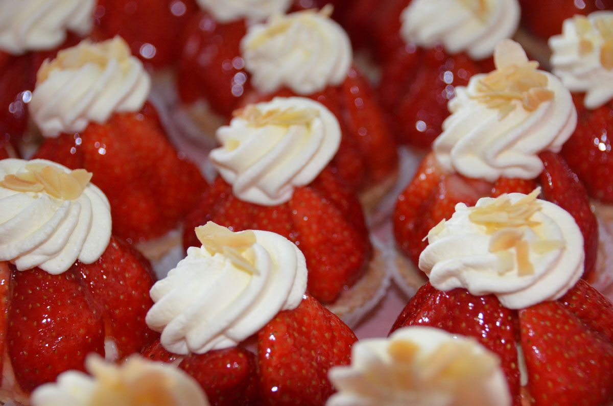 Erdbeeren, garniert mit Tupfen aus weißer Creme und Mandelblättchen, in einer Nahaufnahme eines Desserts
