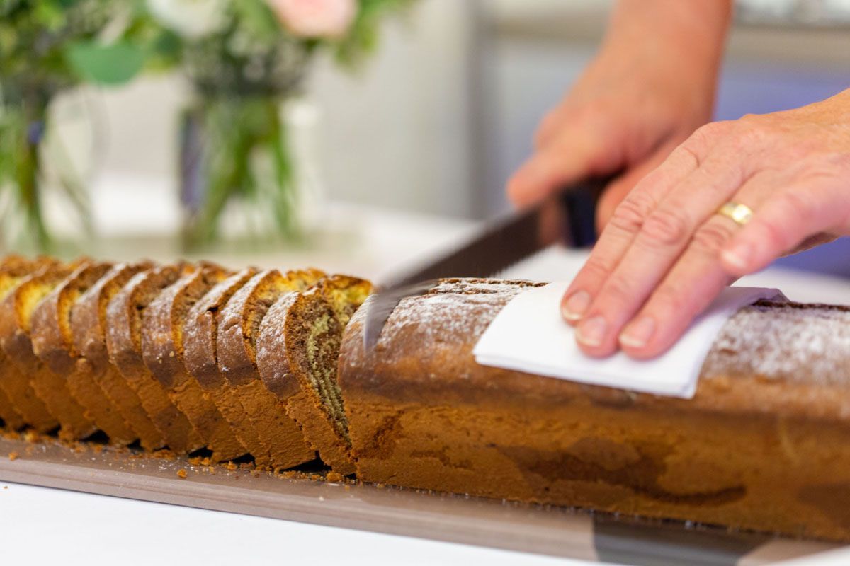 Hände schneiden mit einem Messer einen braunen Baumstammkuchen auf einem weißen Tablett in Scheiben