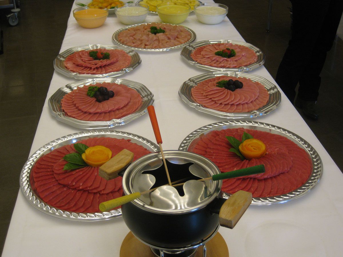 Teller mit rotem Dessert, die auf einem Tisch angerichtet sind, mit einem Fonduetopf und einer Zange im Vordergrund
