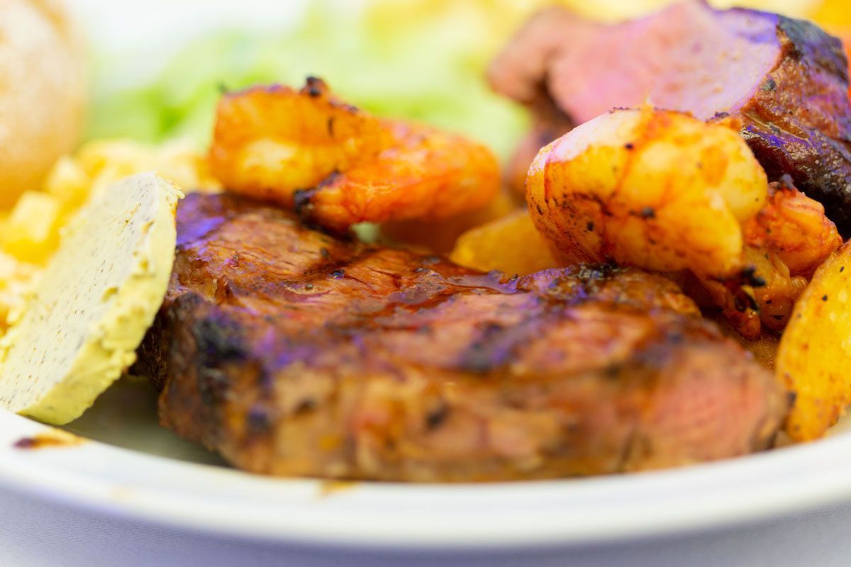 Gegrilltes Steak mit Garnelen und Zitronenspalten auf einem weißen Teller