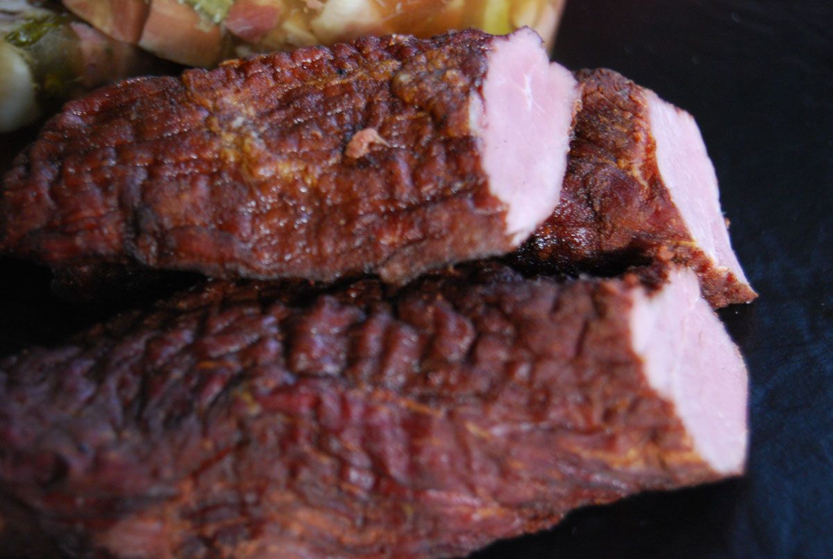 Nahaufnahme von zwei gegrillten Fleischscheiben mit gebräunter Kruste und rosa Kern auf einem dunklen Teller