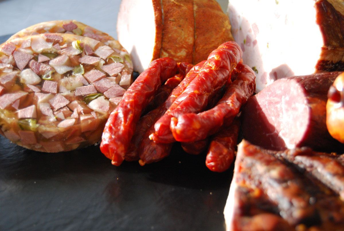 Verschiedene Würste und gepökelte Fleischwaren auf einer dunklen Oberfläche, mit aufgeschnittener Wurst im Vordergrund.
