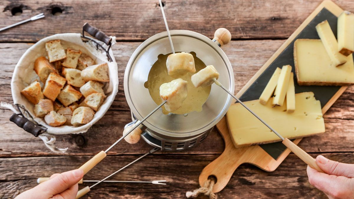 Fonduetopf mit geschmolzenem Käse, Brotwürfeln und Käsescheiben auf einem Holztisch