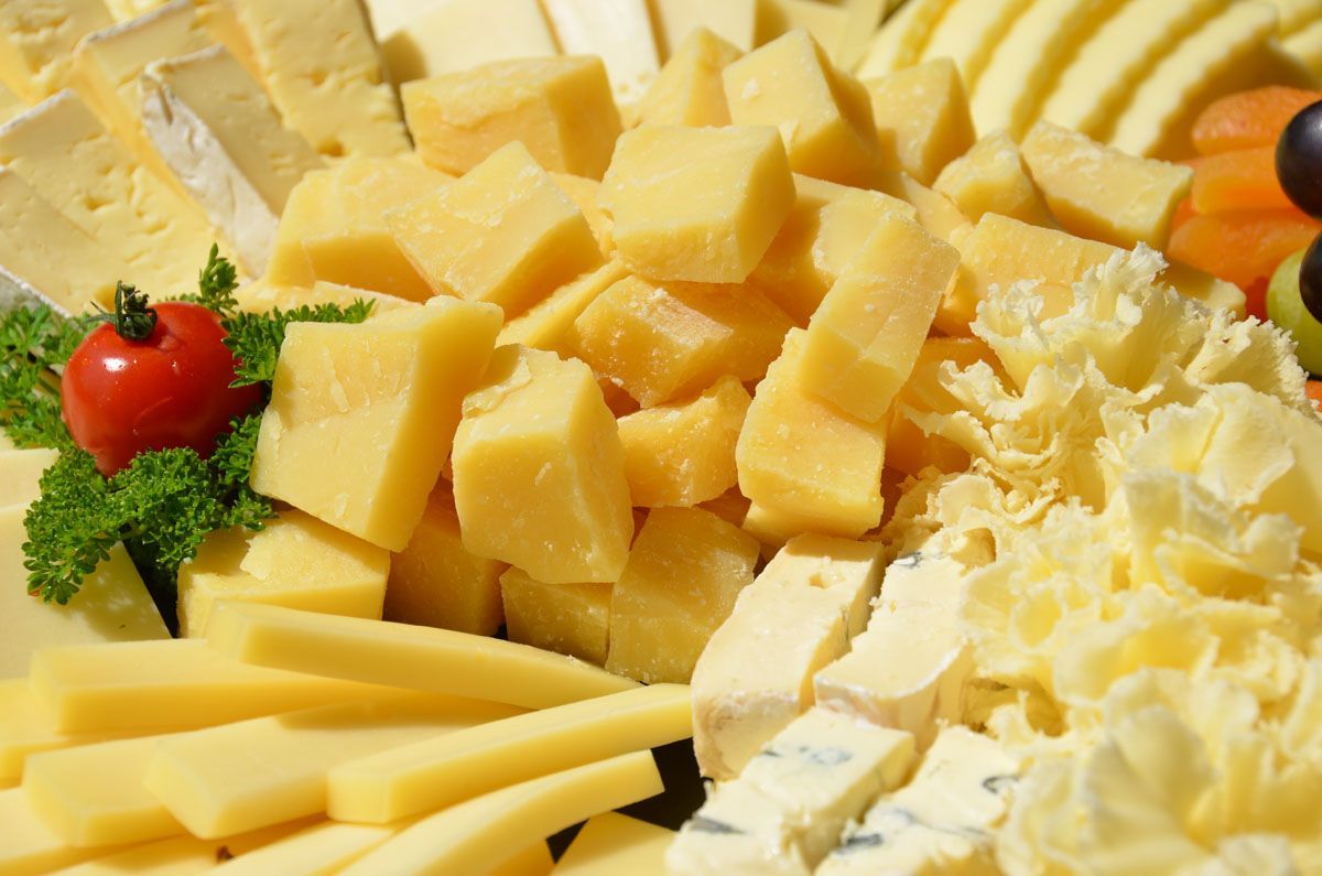 Verschiedene gelbe Käsesorten und Garnierungen auf einer Platte, darunter Stücke, Würfel und geriebener Käse