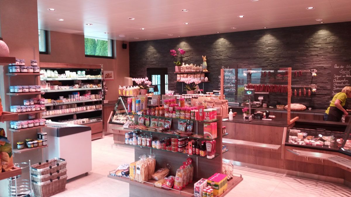 Modernes Bäckerei-Café mit Auslagen, Regalen voller Süßigkeiten und einer Mitarbeiterin hinter der Theke