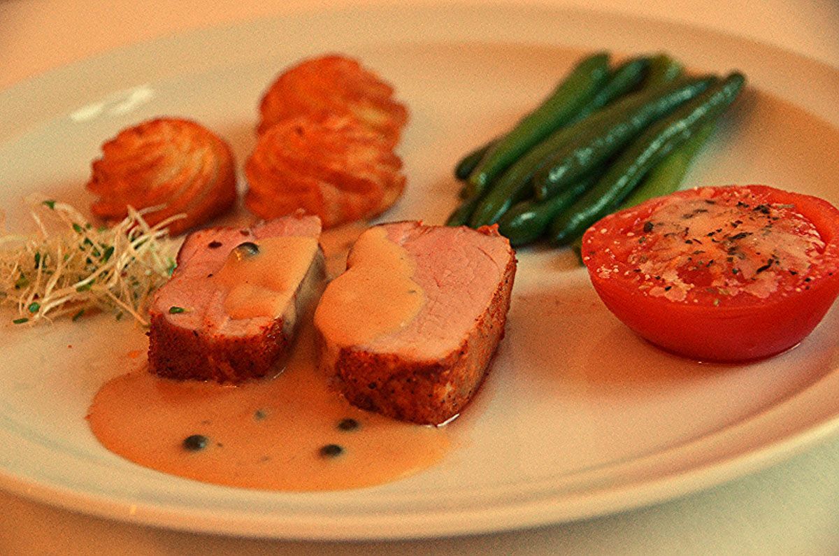 Gourmetgericht mit aufgeschnittenem Fleisch, Kartoffeln, grünen Bohnen und einer gefüllten Tomate als Garnitur