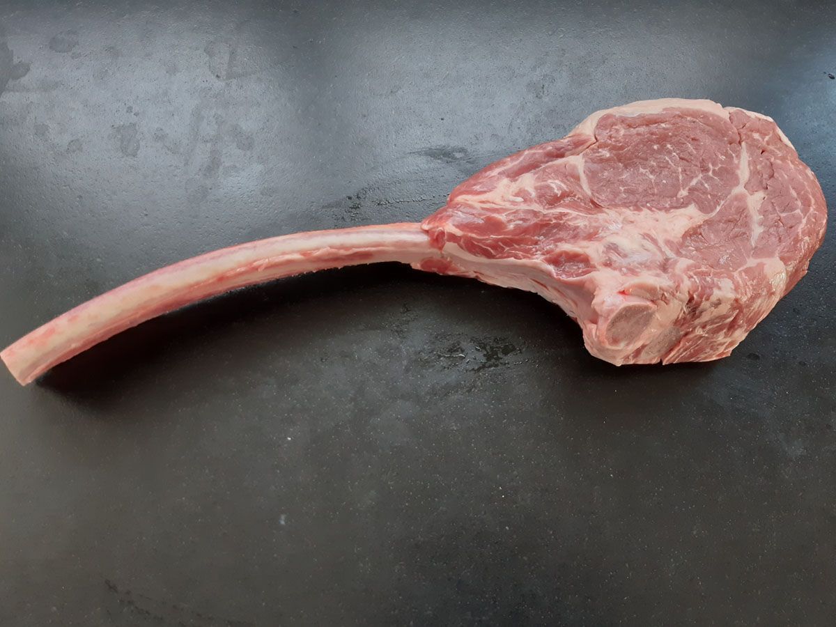 Rohes Tomahawk-Ribeye-Steak mit langem Knochen auf dunklem Untergrund