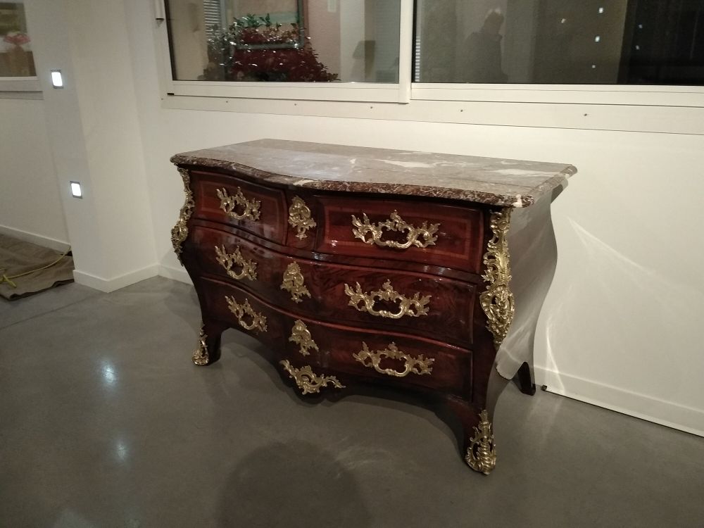 Une commode ornée, à façade serpentine, avec un plateau en marbre, du bois sombre et des ornements en bronze doré.