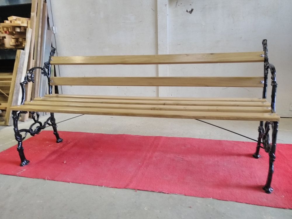 Dans un atelier, un banc public en bois aux pieds en métal noir.