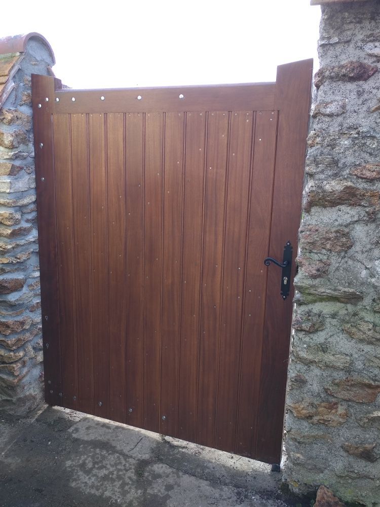 Un portail fermé en bois sombre avec une poignée noire, placé entre deux murs de pierre rustiques.