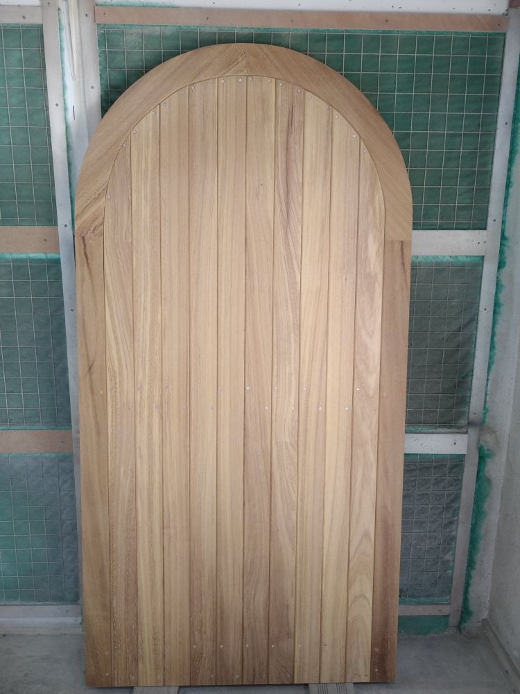 Porte cintrée en bois composée de planches verticales, présentée ici dans une finition naturelle claire avant installation.