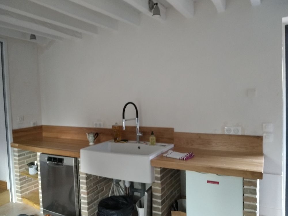 Un comptoir de cuisine rustique avec des surfaces en bois clair, des supports en briques, un évier de ferme blanc et un lave-vaisselle en acier inoxydable.