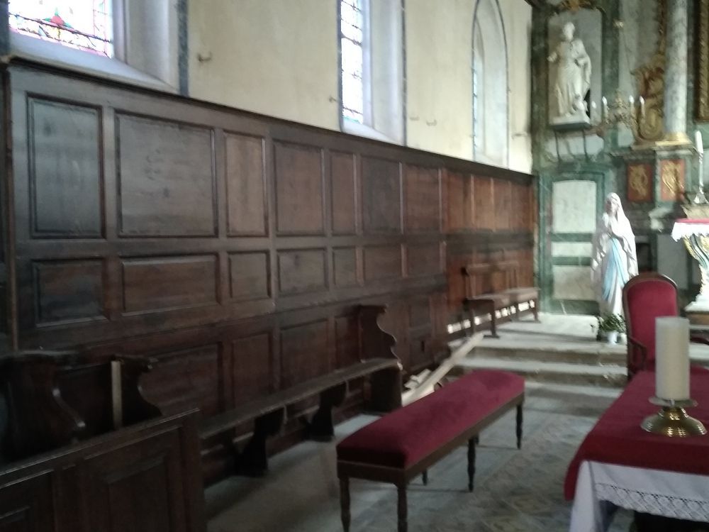 L'intérieur d'une église en bois, avec de longs bancs, des lambris, des statues et un petit autel.
