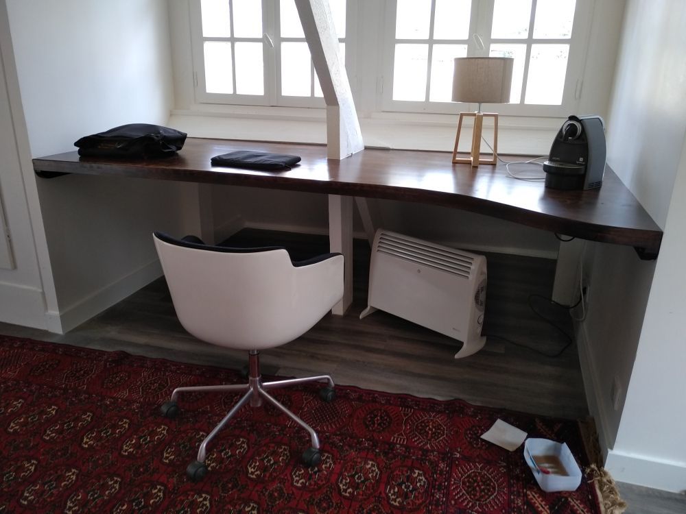 Un bureau avec une chaise blanche, placé devant une fenêtre avec une lampe et un radiateur en dessous.