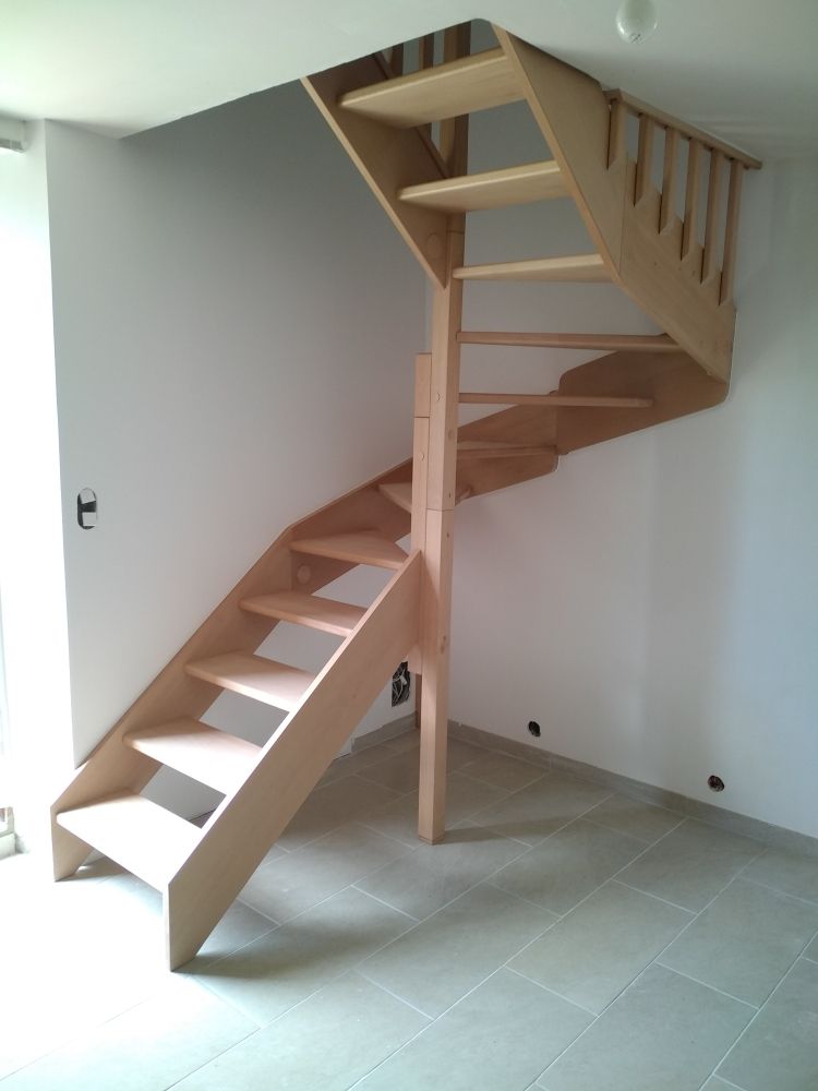 Un escalier en bois clair en forme de L, au design ouvert, installé dans une pièce moderne aux murs blancs et au sol carrelé gris.