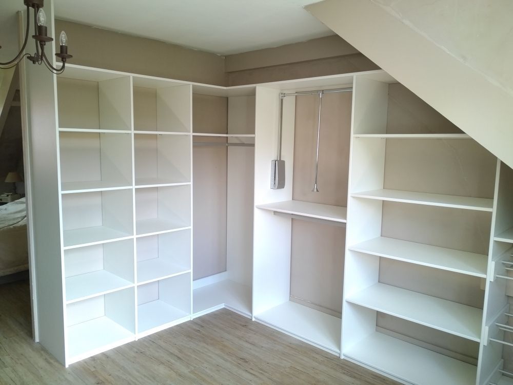 Un ensemble d'étagères et de rangements de placard blancs, fabriqués sur mesure, installés en forme de L contre un mur sous un plafond incliné.