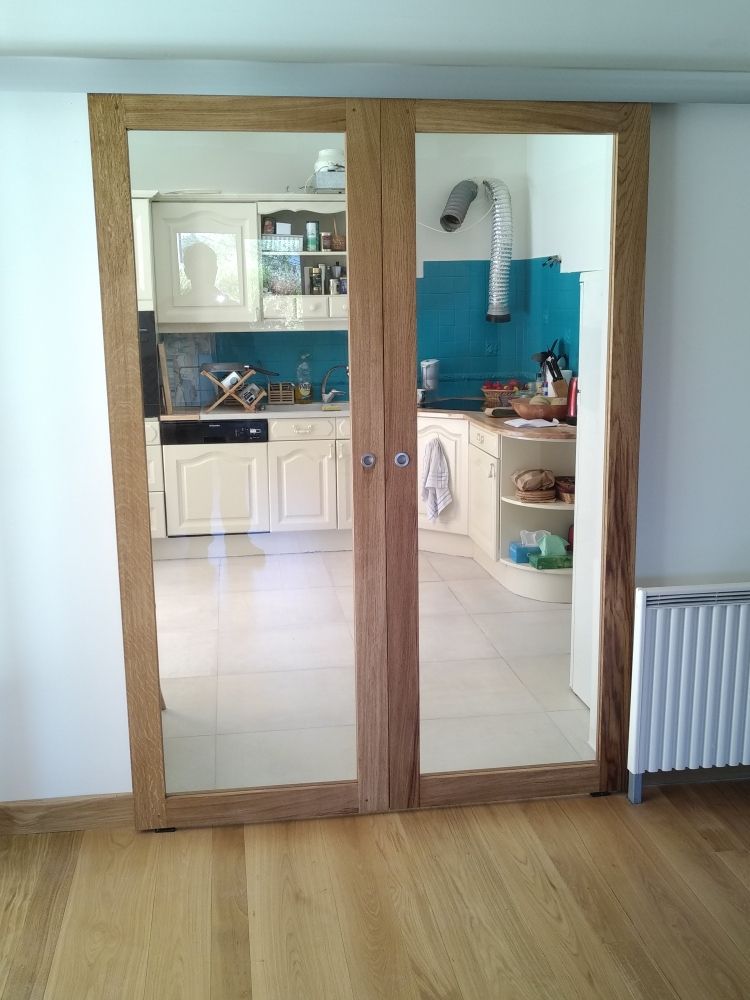 Deux portes vitrées à cadres en bois clair donnent sur une cuisine aux armoires claires et à la crédence bleue.
