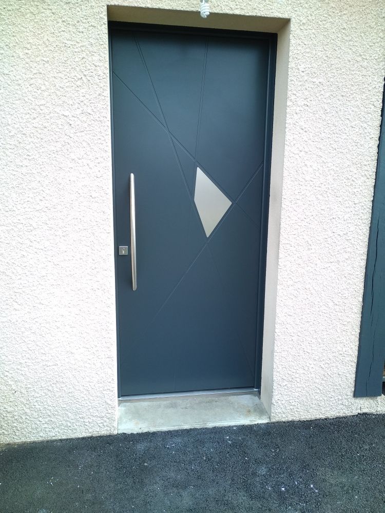 Une porte extérieure moderne gris foncé avec une poignée verticale argentée et une unique découpe géométrique en verre dans un mur texturé.