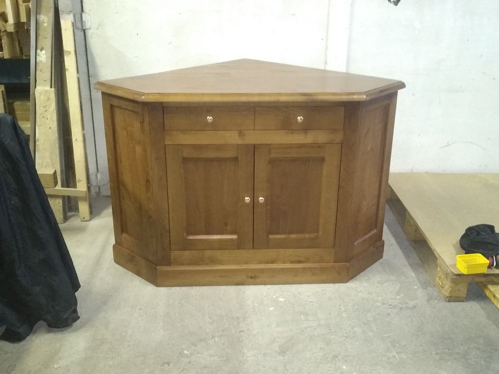 Un meuble d'angle en bois avec deux tiroirs et deux portes, placé dans un atelier inachevé.